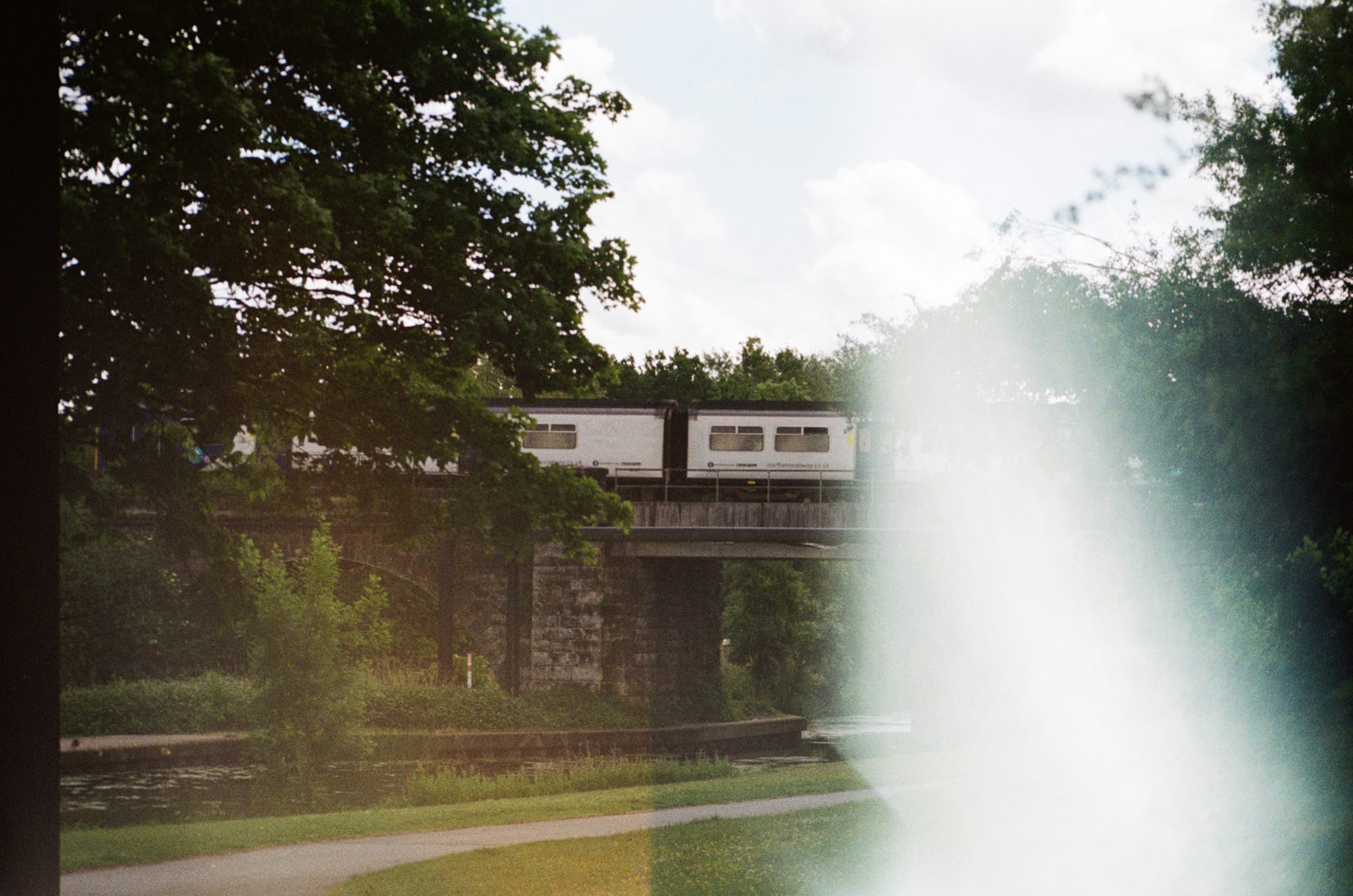 Film photo but most of the image has a white blur invading most of it. Though a train can be seen crossing a bridge with trees either side of the image.