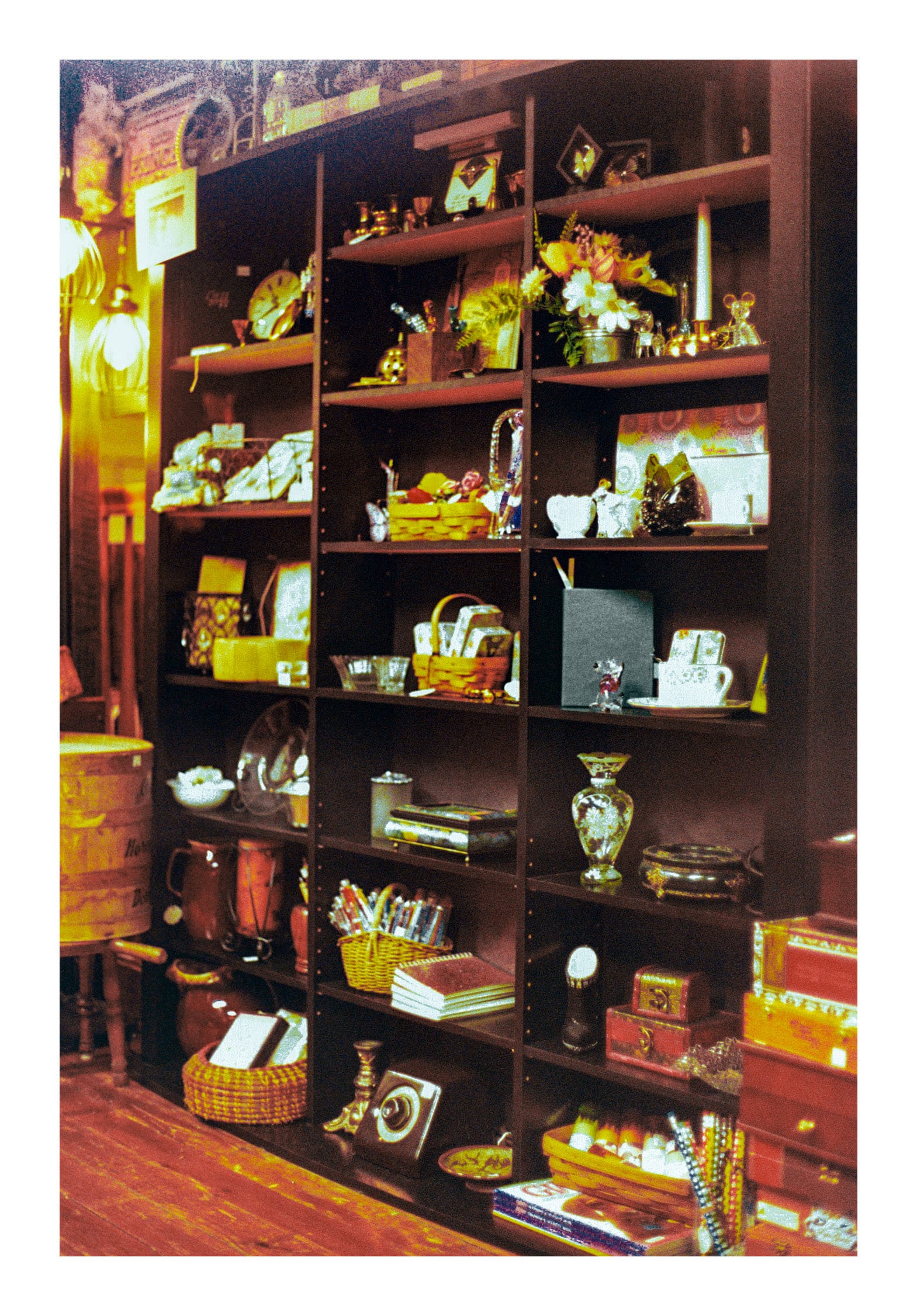 Film photo of a bookshelf with a variety of antique items such as vases, baskets and flowers