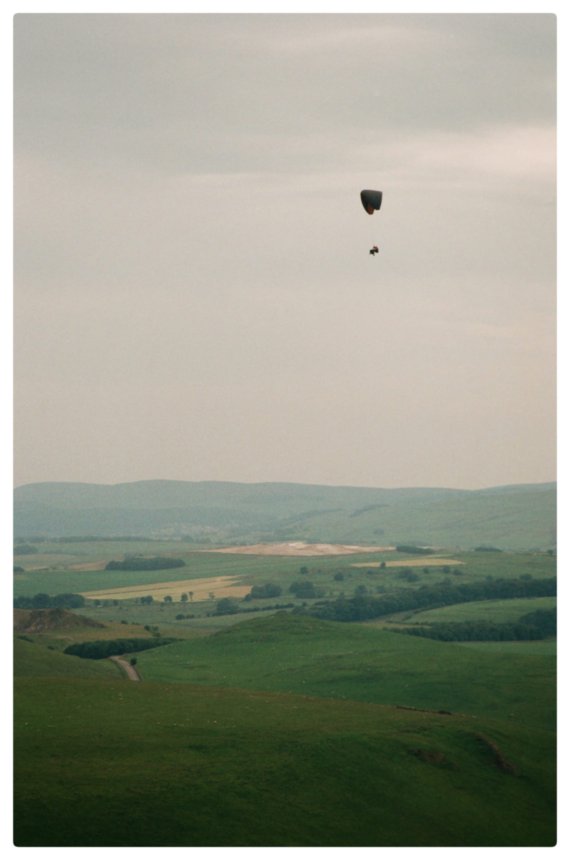 Film picture of a paraglider paragliding over the view of the peak of Mam Tor in overcast skies in the Peak District