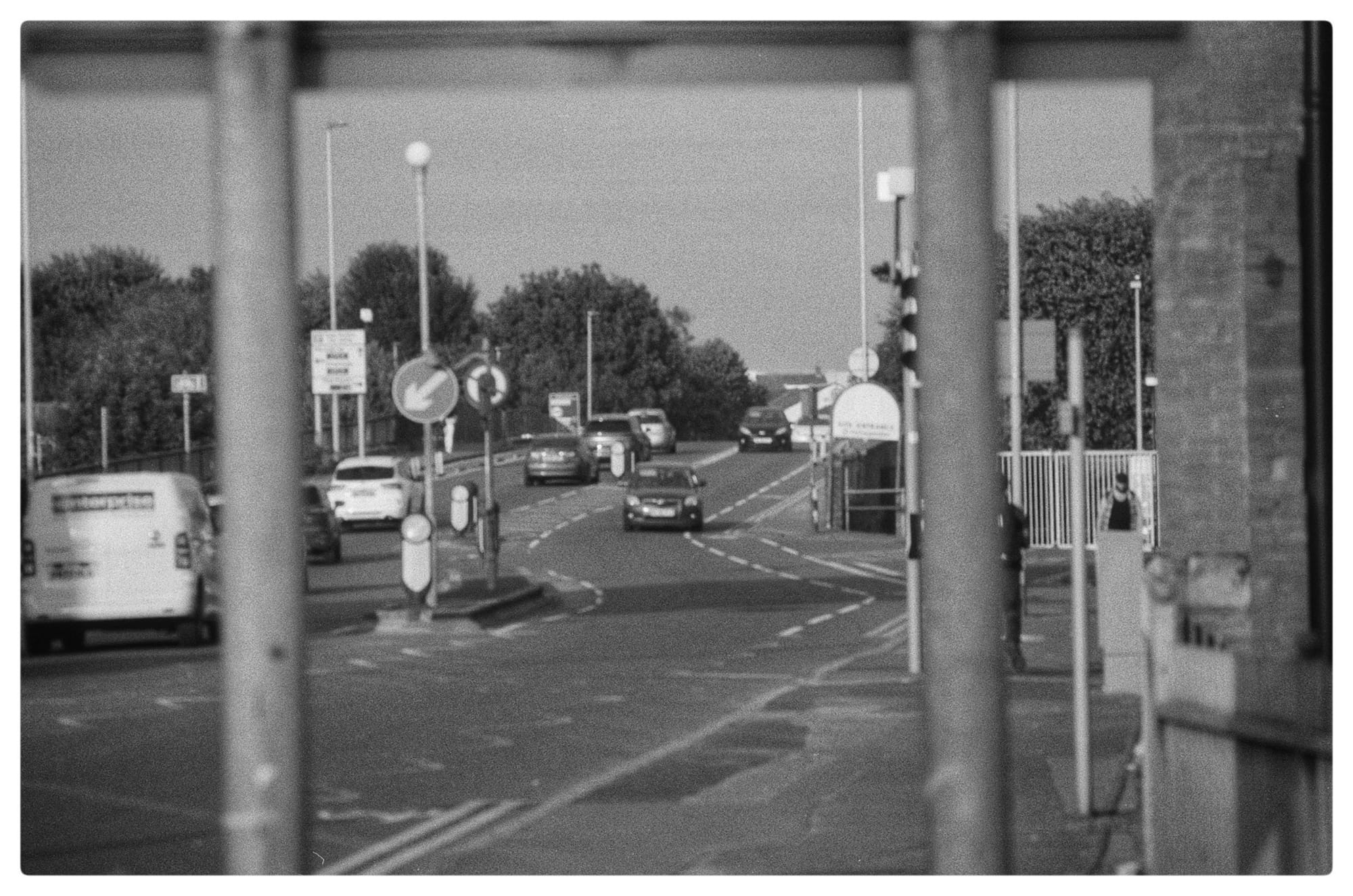 Black and white photo of a road with a car between two poles for a sign acting as a picture frame