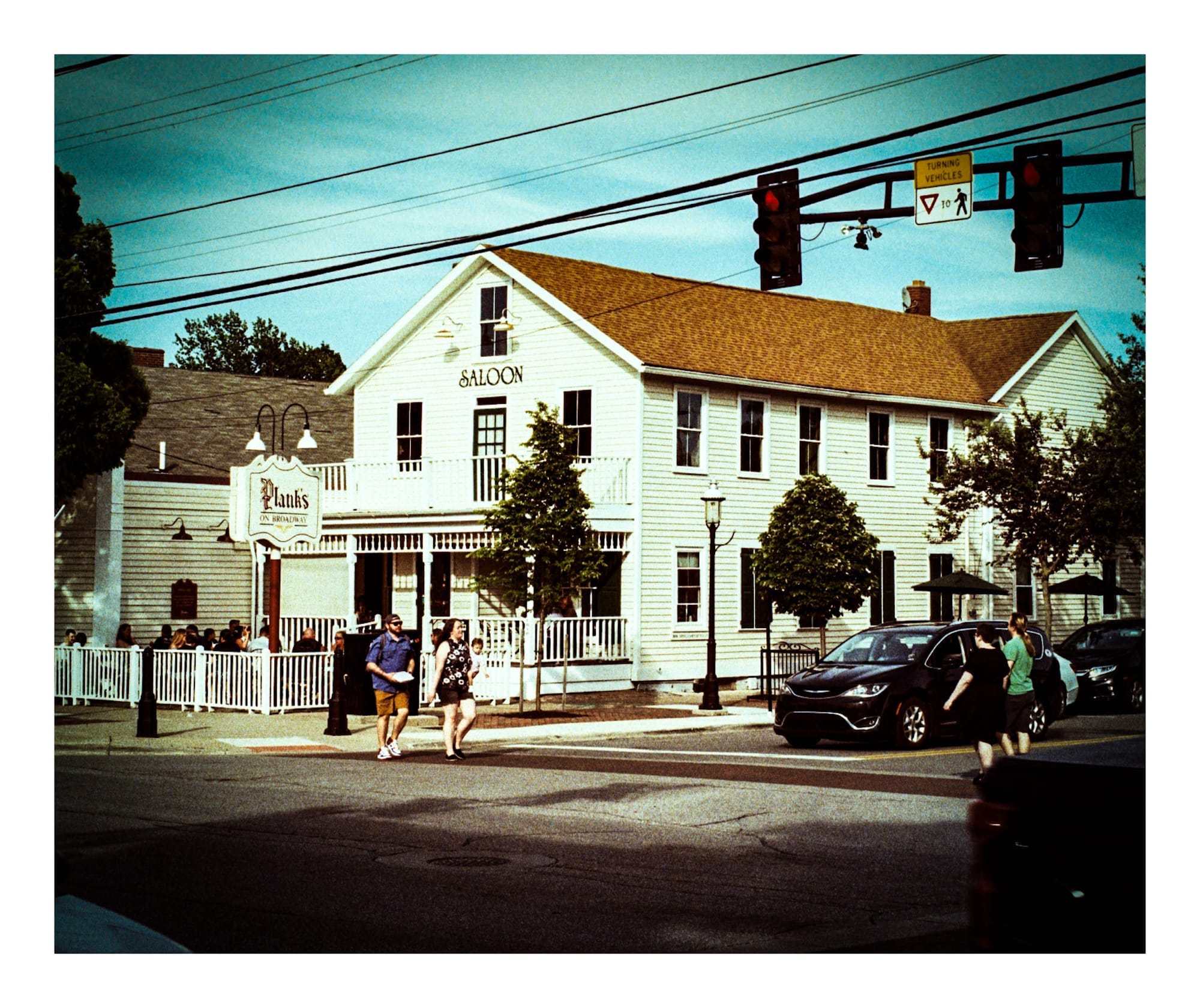 Film photo of a saloon building, taken from a intersection with pedestrians crossing on a red light.